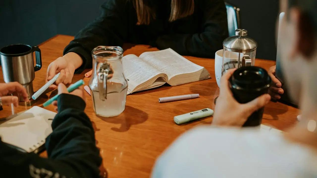 A small group around a wooden table with open Bibles and coffee