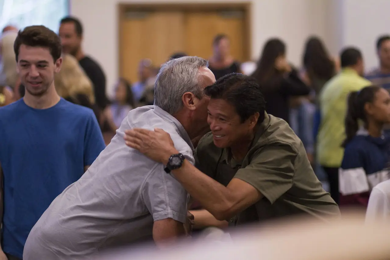Two men greeting each other with a hug in a church lobby