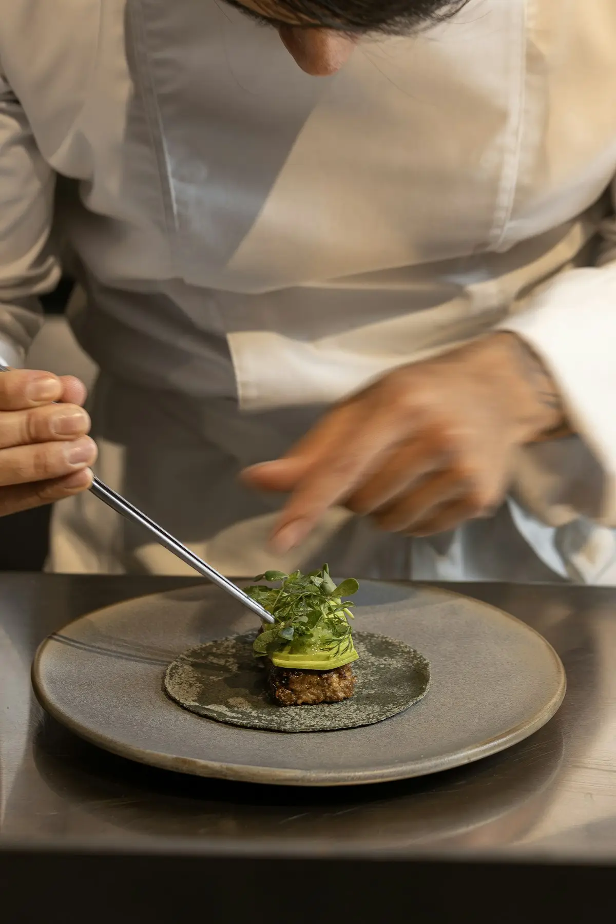A chef plating a dish with tweezers