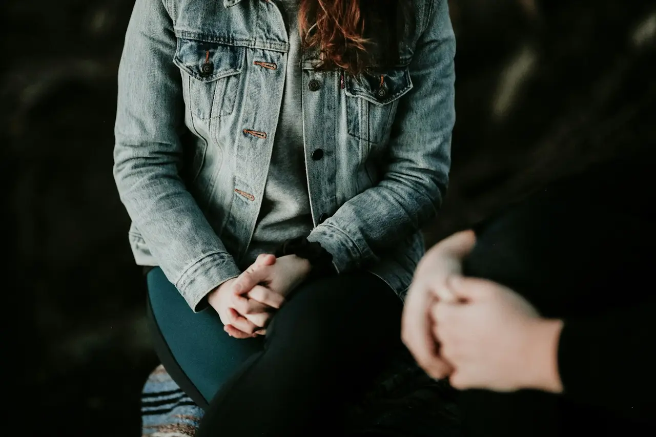 A client's hands clasped, sitting across from a therapist