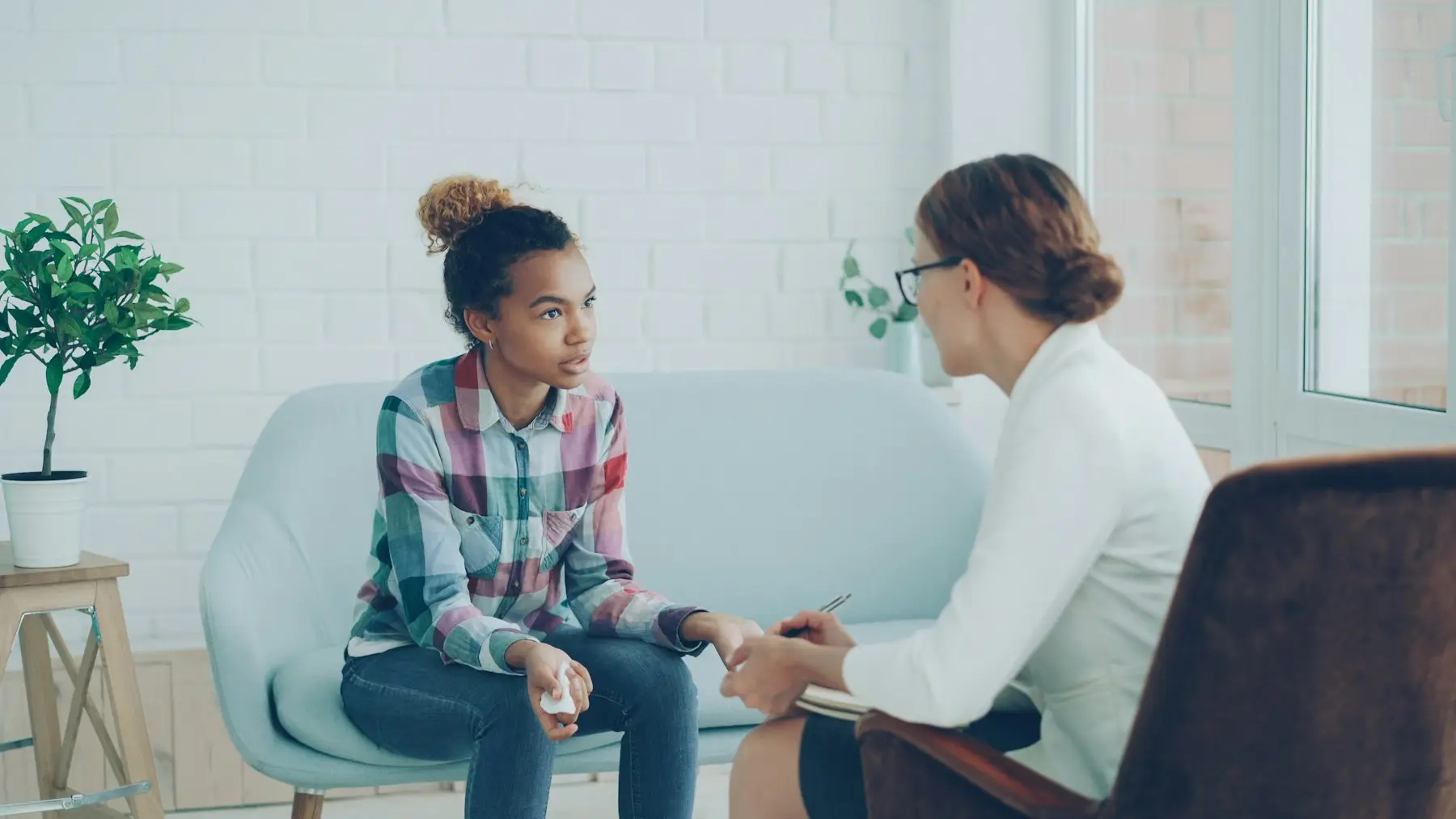 A therapist talking with a young woman on a couch in a bright office